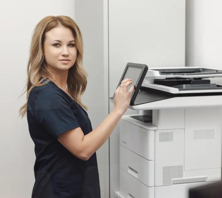 Blondynka w ciemnym uniformie obsługująca drukarkę w recepcji Centrum Medycznego Alma Med