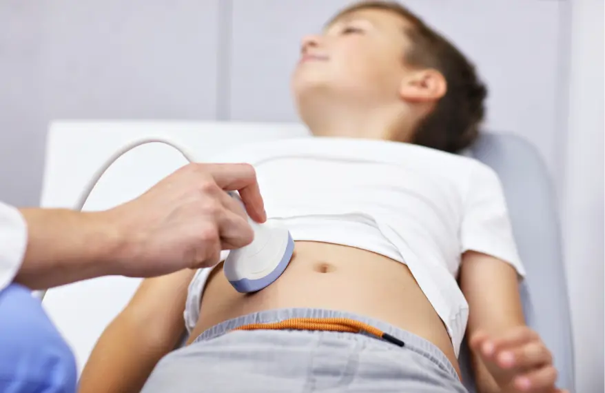 Radiolog przeprowadza badanie USG brzucha chłopca, który leży na leżance lekarskiej.