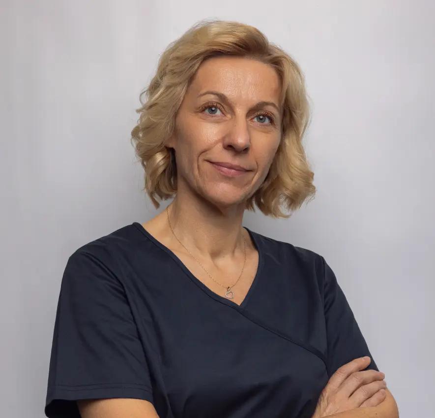 Uśmiechnięta pielęgniarka z krótkimi blond włosami w ciemnym uniformie na szarym tle