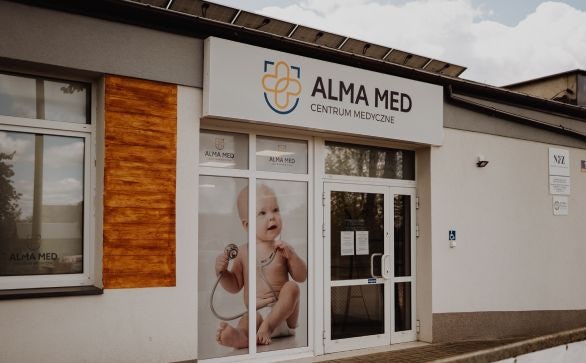 Budynek przychodni Alma Med z logo nad wejściem, na oknach przyklejona jest folia z bobasem, co nawiązuje do medycyny rodzinnej.