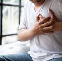 Mężczyzna w białej koszulce i spodniach jeansowych, który trzyma się za klatkę piersiową, co sugeruje ból i chorobę serca
