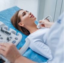 Kobieta leżąca na leżance lekarskiej i lekarz radiolog w białym fartuchu, który przeprowadza badanie USG tarczycy